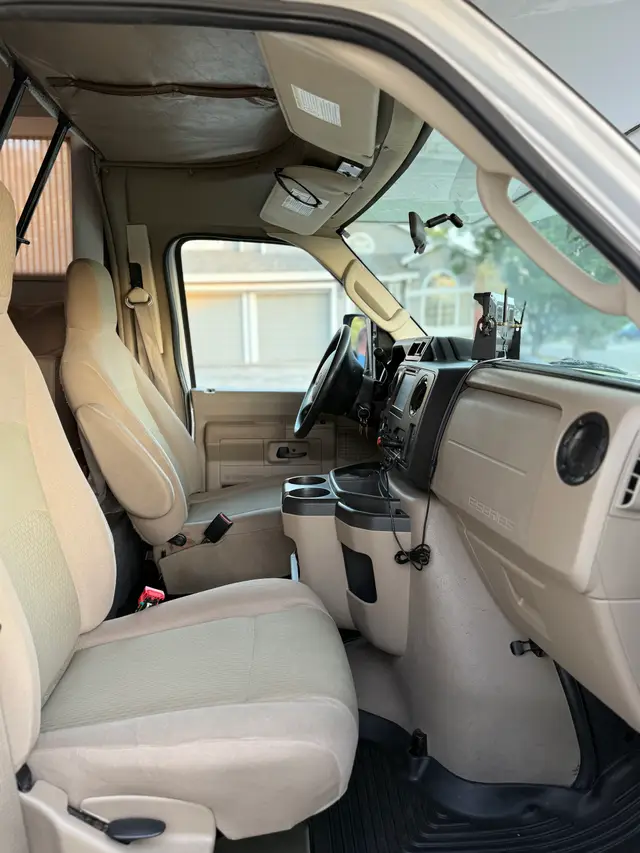 RV front cab showing two tan captain’s chairs and center console with cup holders.