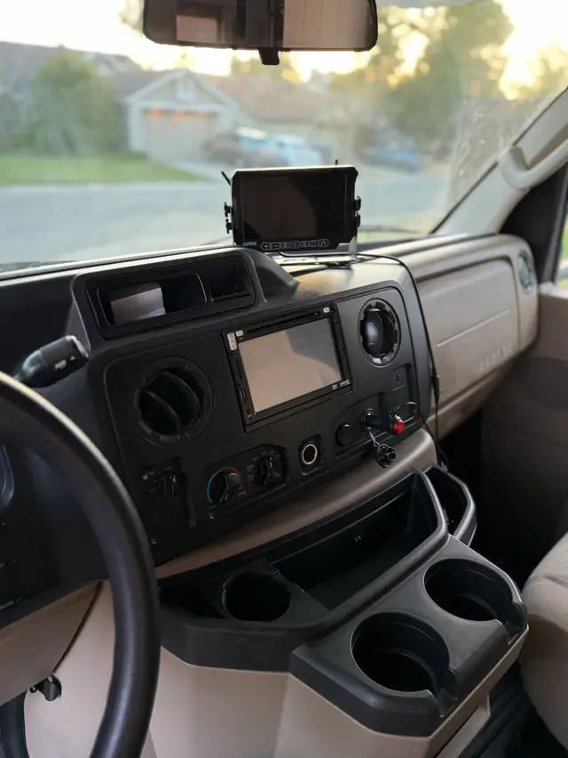 RV driver cockpit with dashboard display, touchscreen unit, and multiple cup holders.