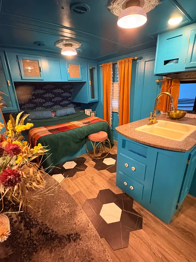 Colorful RV bedroom with turquoise cabinets, green bedding, and kitchen peninsula in foreground.