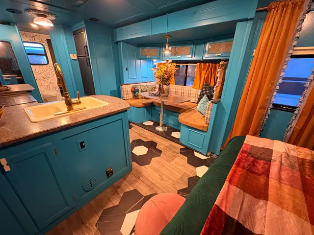 Turquoise RV kitchen with peninsula sink facing a wraparound dinette and patterned flooring.