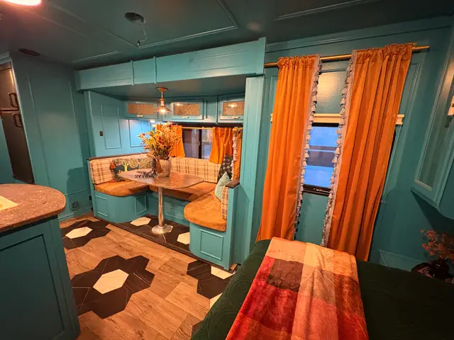 Turquoise RV dining nook with wraparound bench, orange curtains, and hexagon inlay flooring.