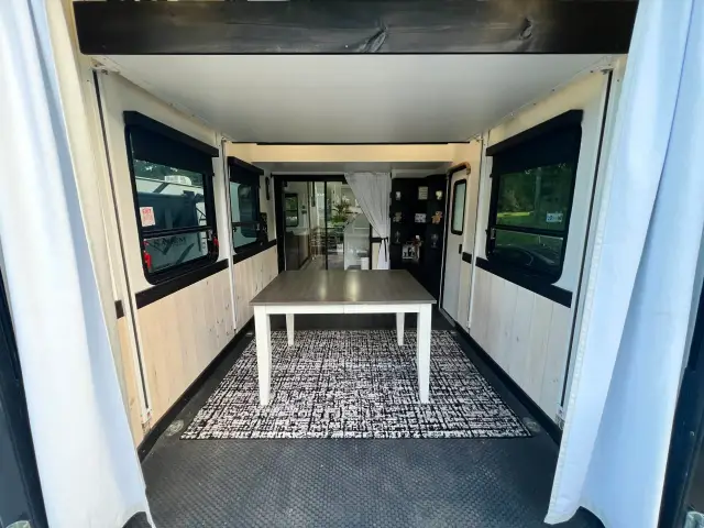 Toy hauler garage converted to dining area with table, rug, and windows leading toward main RV interior.