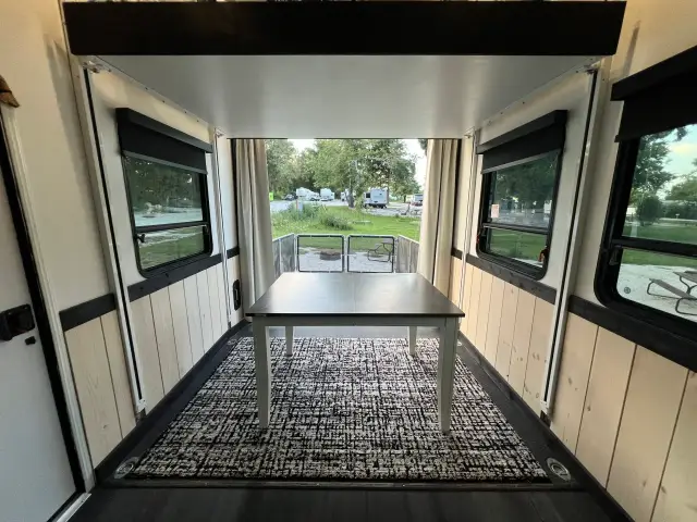 View from toy hauler garage dining area out to fenced rear patio deck at a campground.