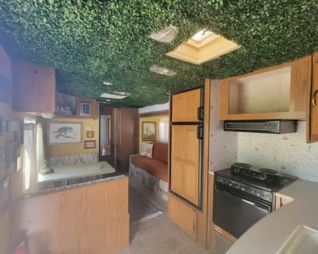 RV kitchen with wood cabinets, fridge, range, and view into dinette and lounge.
