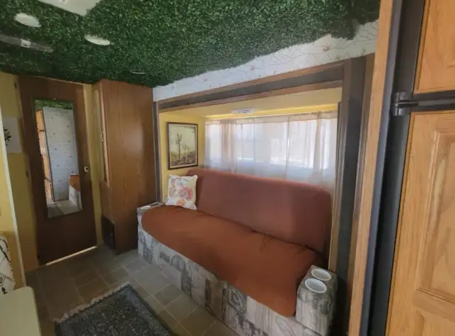 RV lounge area with sofa, large window, and mirrored door under a green ceiling.