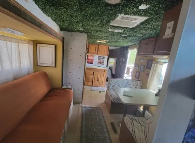 RV living area with sofa, dinette, and kitchen under a green textured ceiling.
