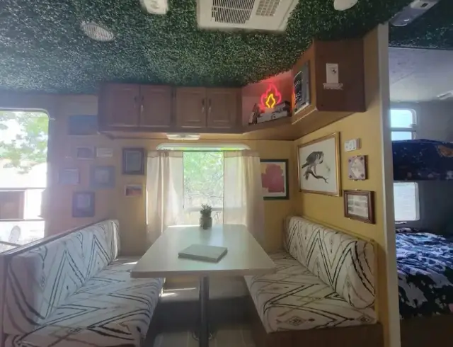 RV dinette with patterned seating, wall art, and adjacent bunk bed area.
