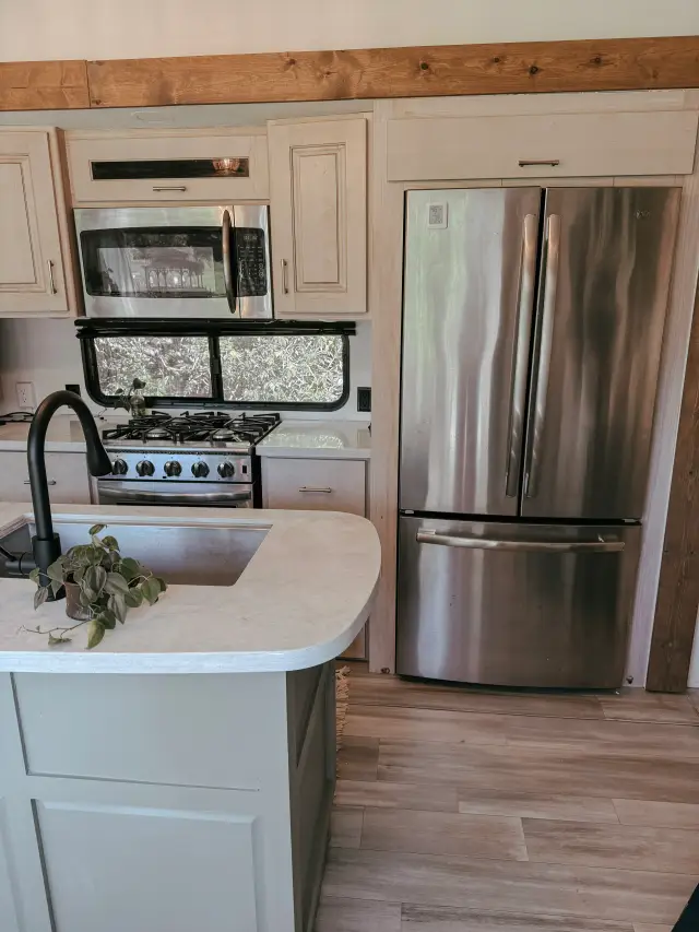 Close view of RV kitchen with stainless french door fridge and stove with microwave.