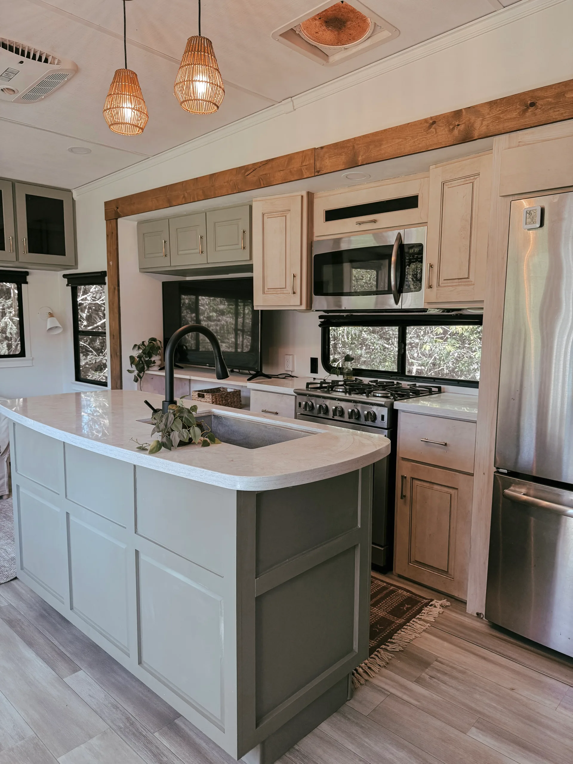 RV kitchen with island sink, gas range, stainless fridge and woven pendant lights.
