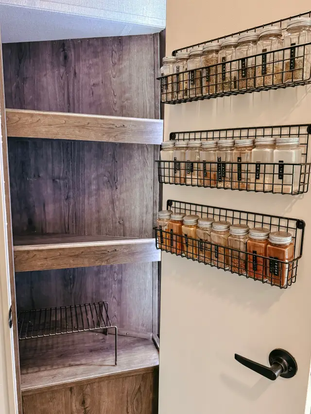 Open RV pantry with wood shelves and spice racks mounted on the door.