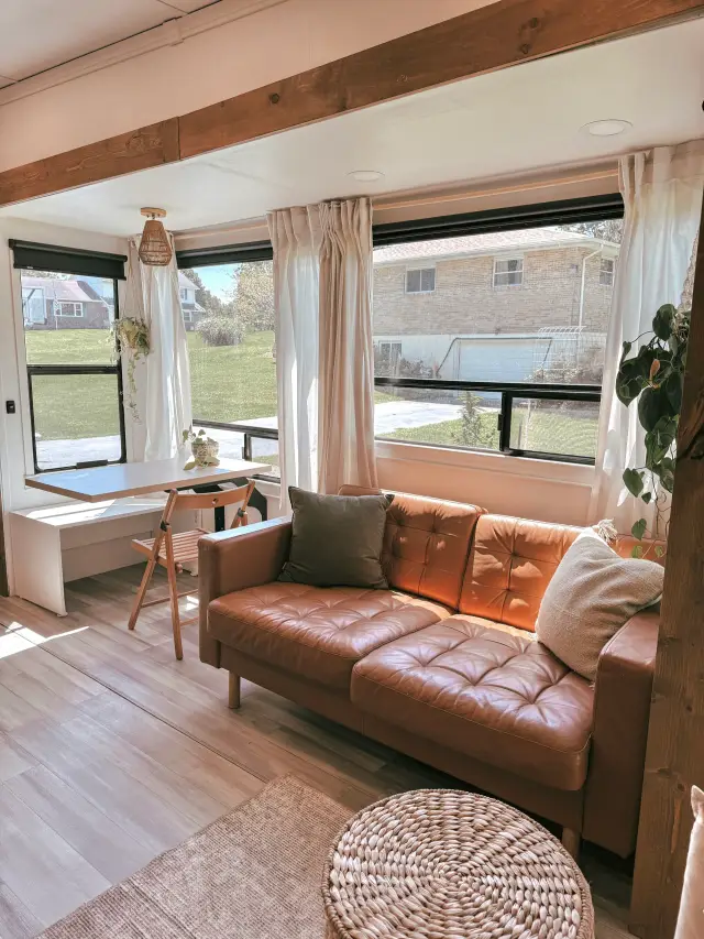 RV living area with leather sofa, wall-mounted table and large curtained windows.
