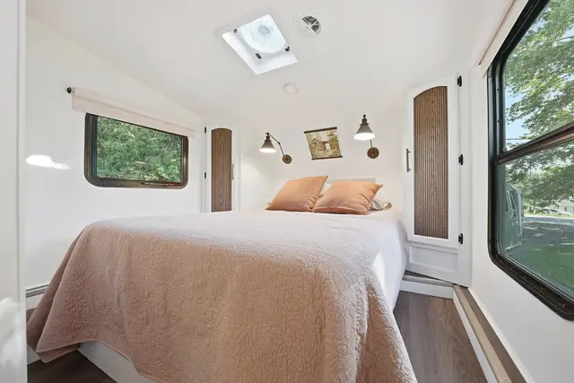 RV front bedroom with blush bedding, side cabinets, and windows on both sides.