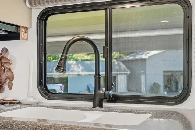 Close-up of RV kitchen sink with black faucet and large window above.