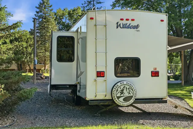 Rear exterior of fifth wheel RV with ladder, slide-out, and spare tire cover.