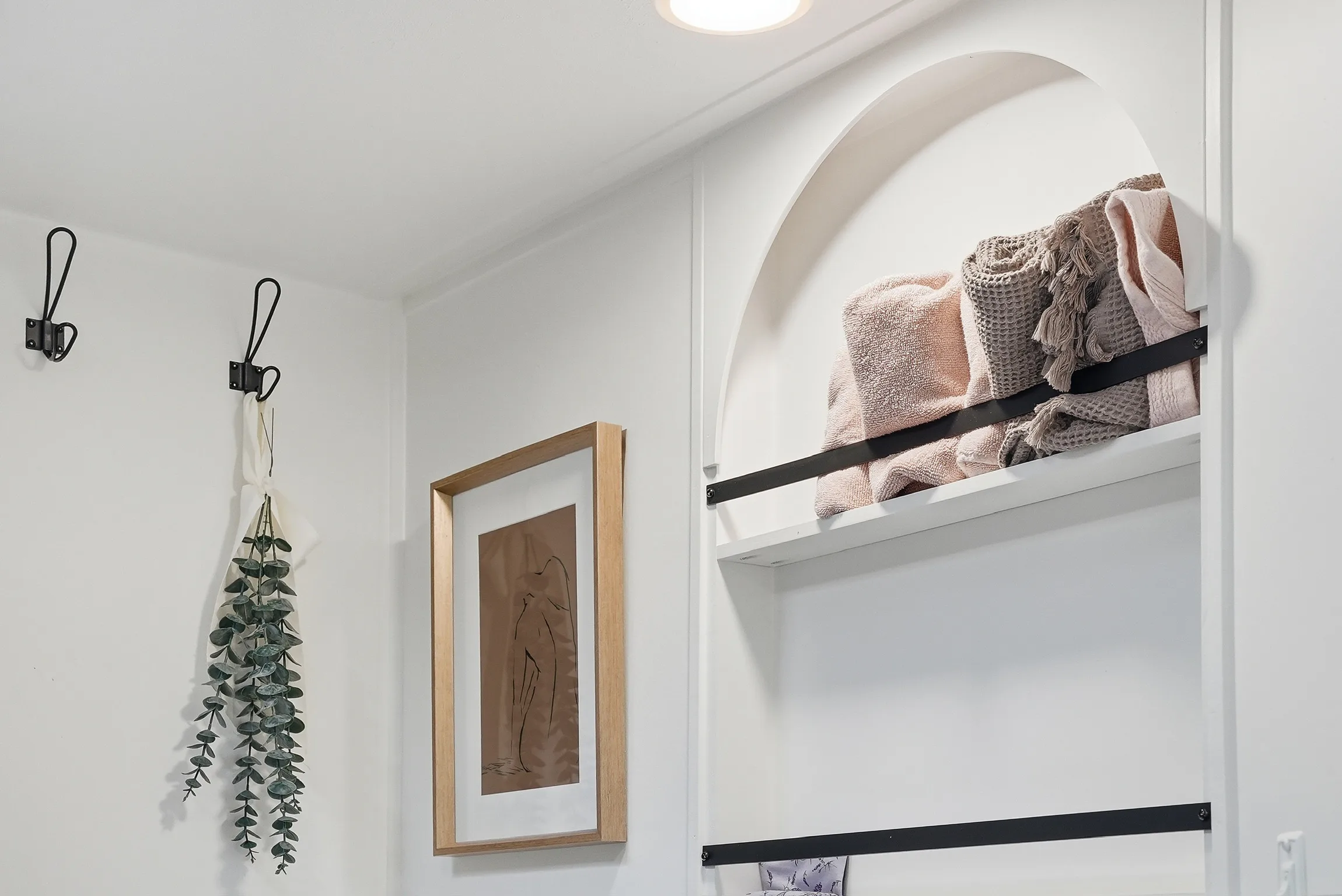 RV bathroom wall with arched built-in shelving, towels, hooks, and framed art.