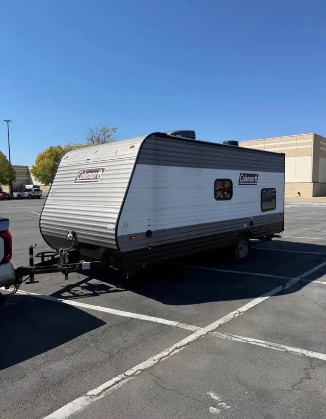 Street-side view of compact travel trailer with roof AC and single axle hitched to a truck.