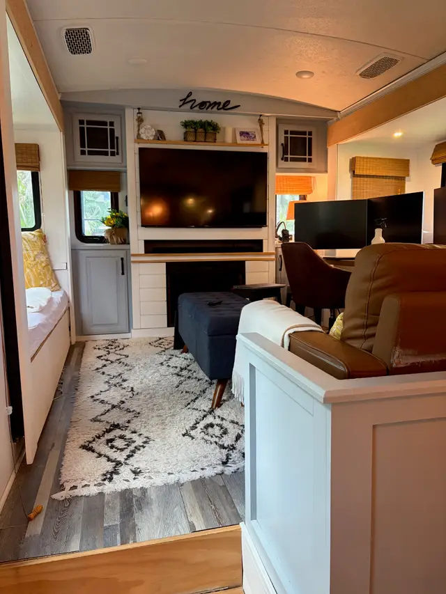 Rear living room of fifth wheel RV with large TV, fireplace, rug and multiple seating areas.