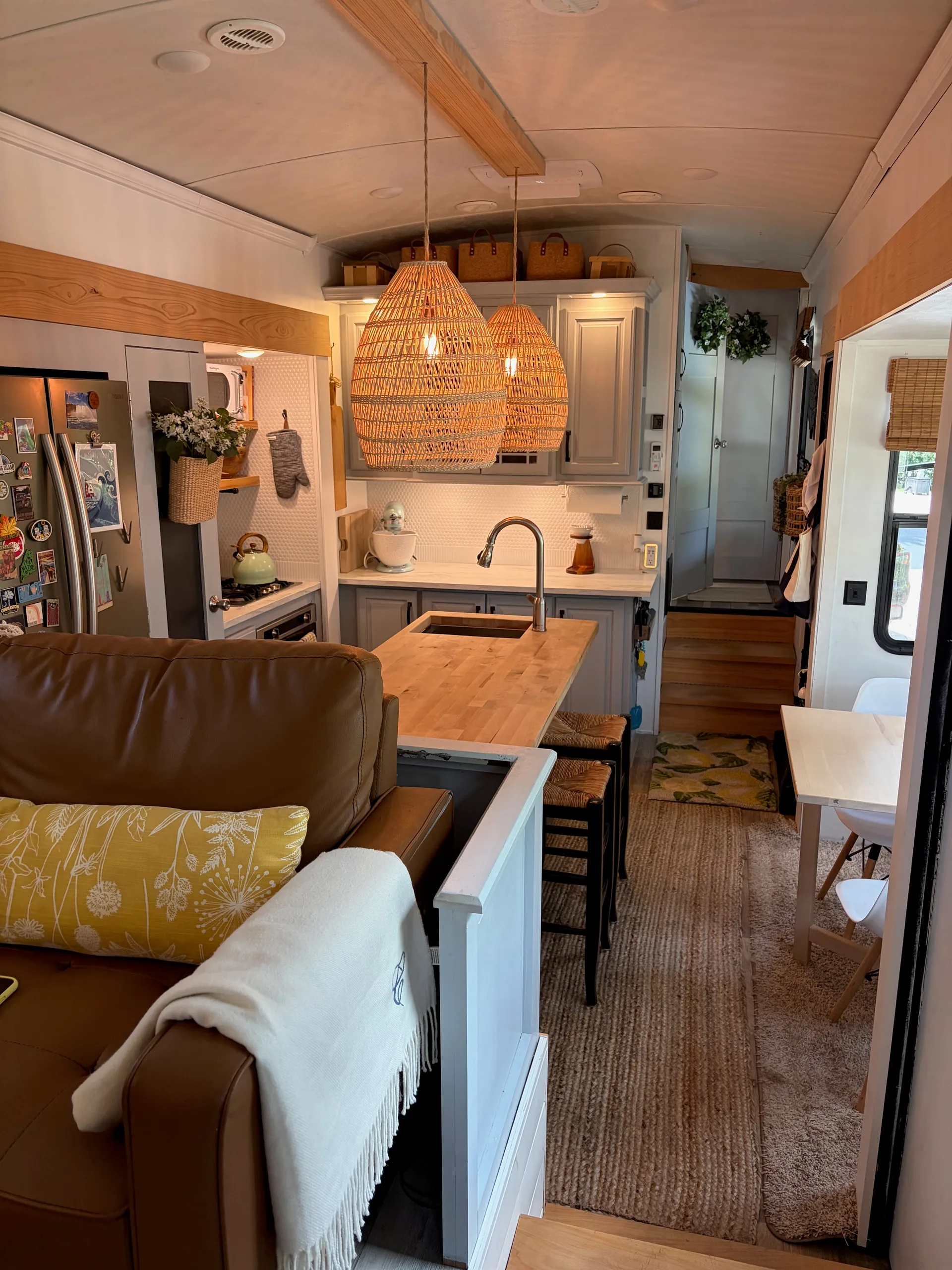 RV kitchen with butcher-block island, woven pendants, gray cabinets and adjacent leather sofa.