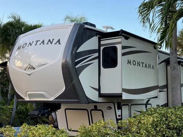 Front exterior of fifth wheel RV with slide-out extended among palm trees.