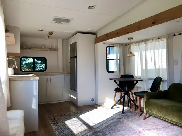 RV kitchen with white cabinets, butcherblock counters, and adjacent dining table with two chairs.