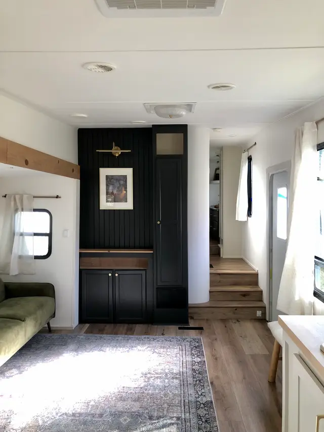 Wide view of RV living room with black feature cabinet, rug, and steps to upper level.