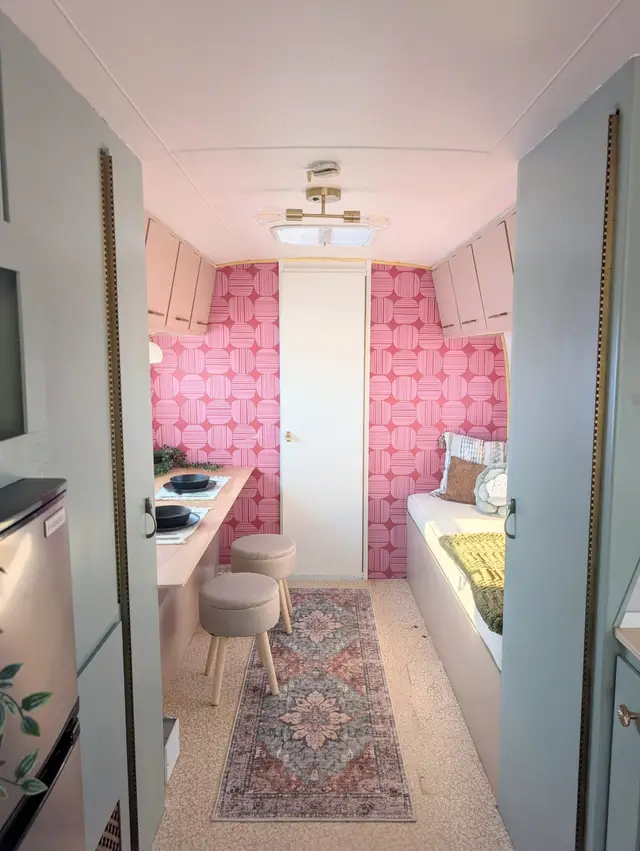 Rear of travel trailer with pink accent wall, desk with stools, and bench seating.