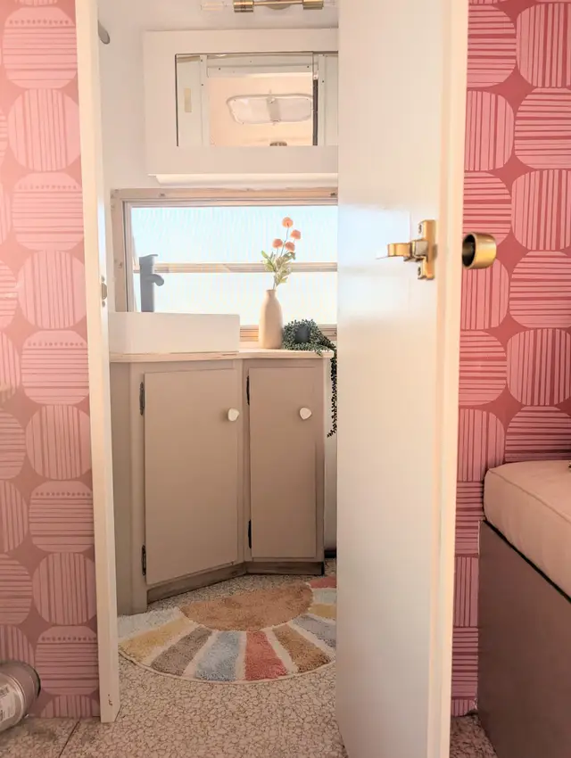 Hallway view into RV bathroom with corner vanity, vessel sink, and large window.