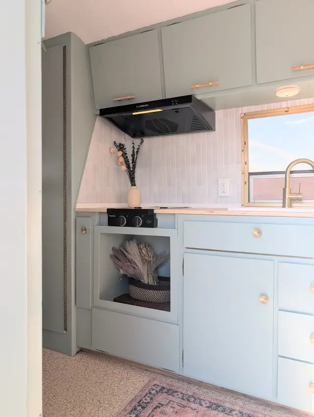 Closeup of mint green RV kitchen with two burner cooktop, range hood, and tile backsplash.